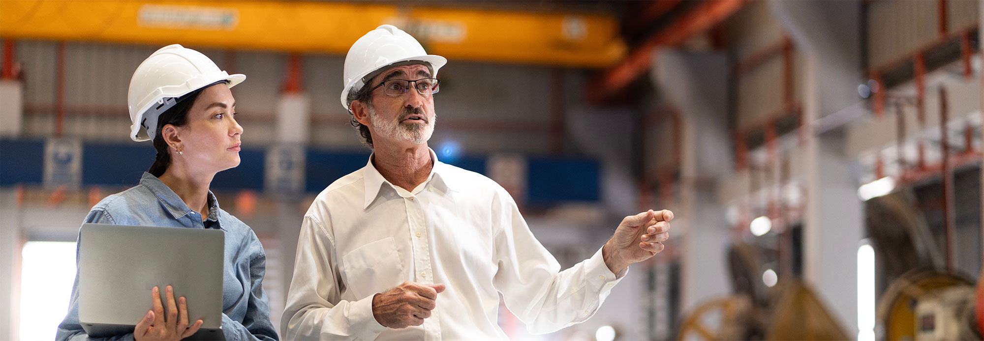 two professional engineer,worker,technician use clipboard discuss work, walk in steel metal manufacture factory plant industry. Black African American man and woman wear hard hat check quality machine